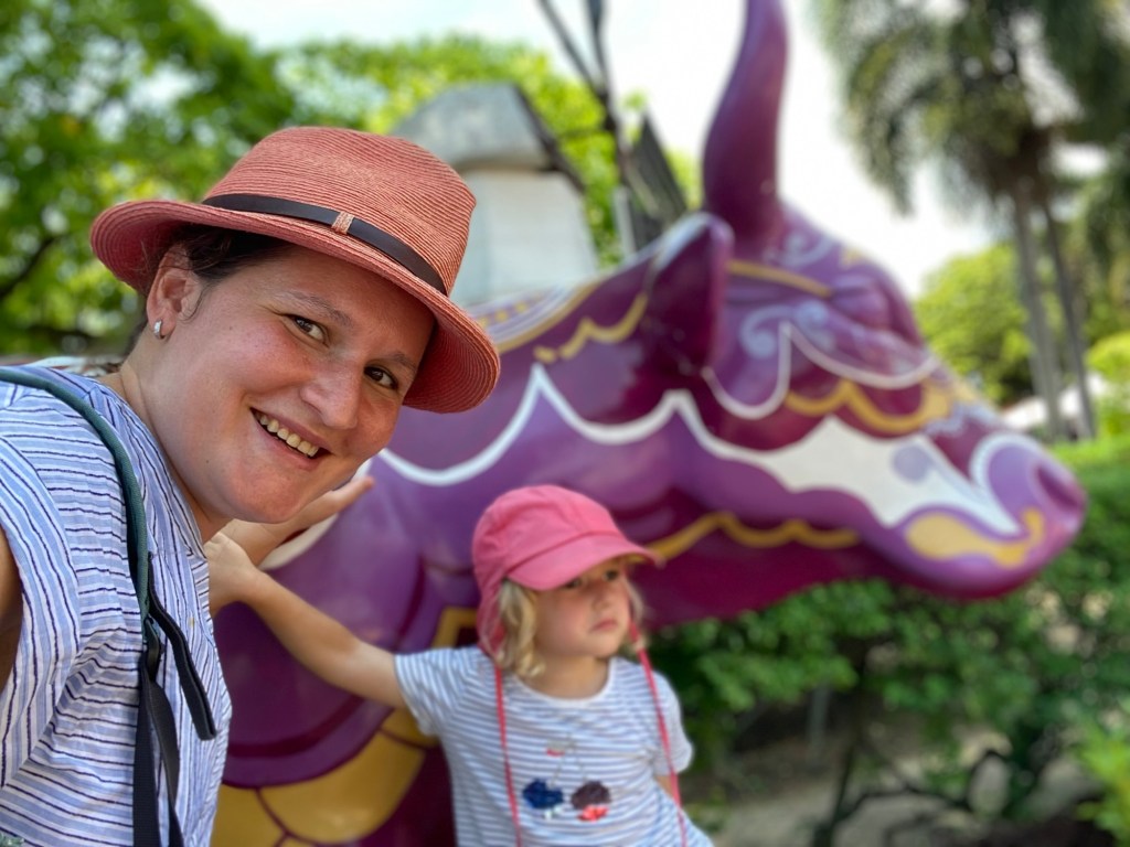 A woman and a child posing for a selfie with a large, colorful dragon sculpture in the background.